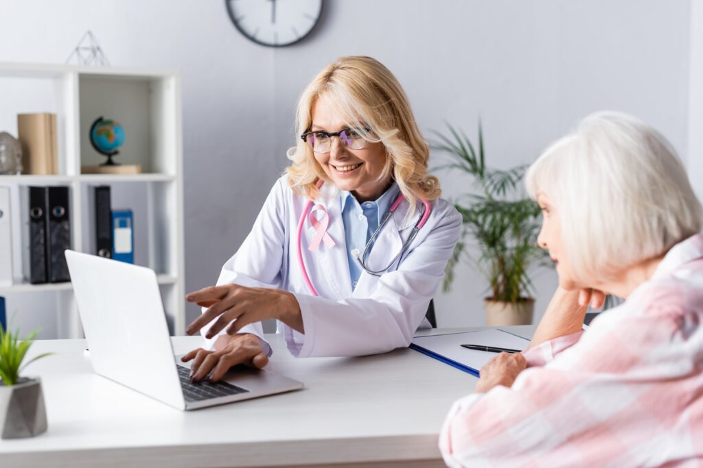 Smiling doctor talking to senior woman, motioning to laptop