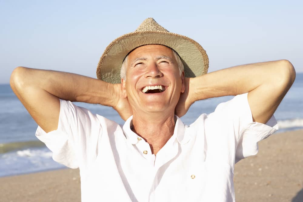 Smiling senior man with arms behind head at beach