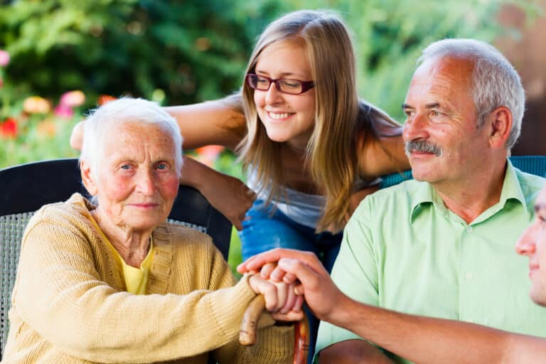 Smiling young woman, older man, and elderly woman sitting outside