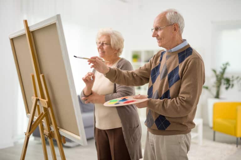 Two seniors painting on canvas using easel