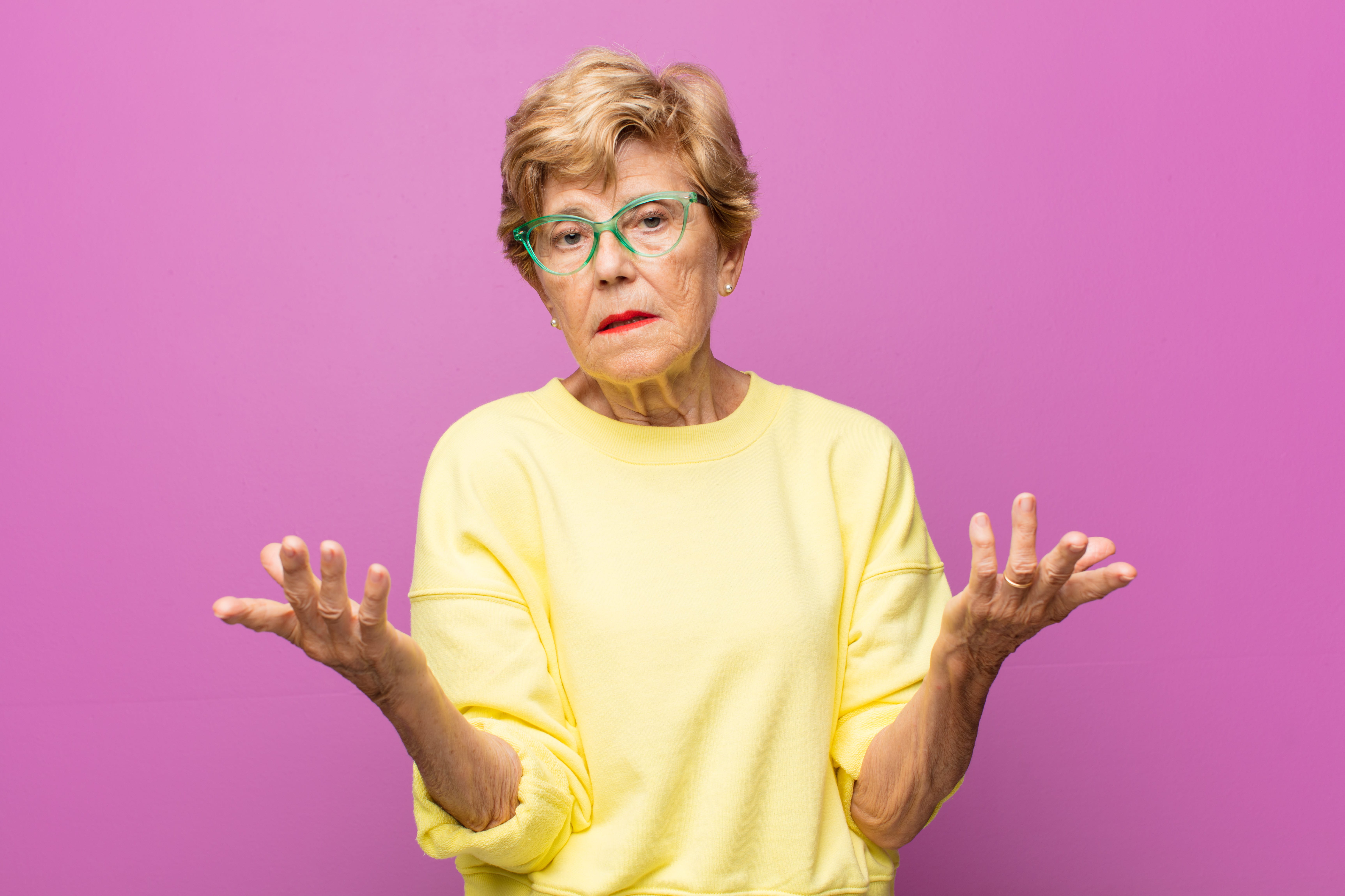 Senior woman holding hands up, confused, magenta background