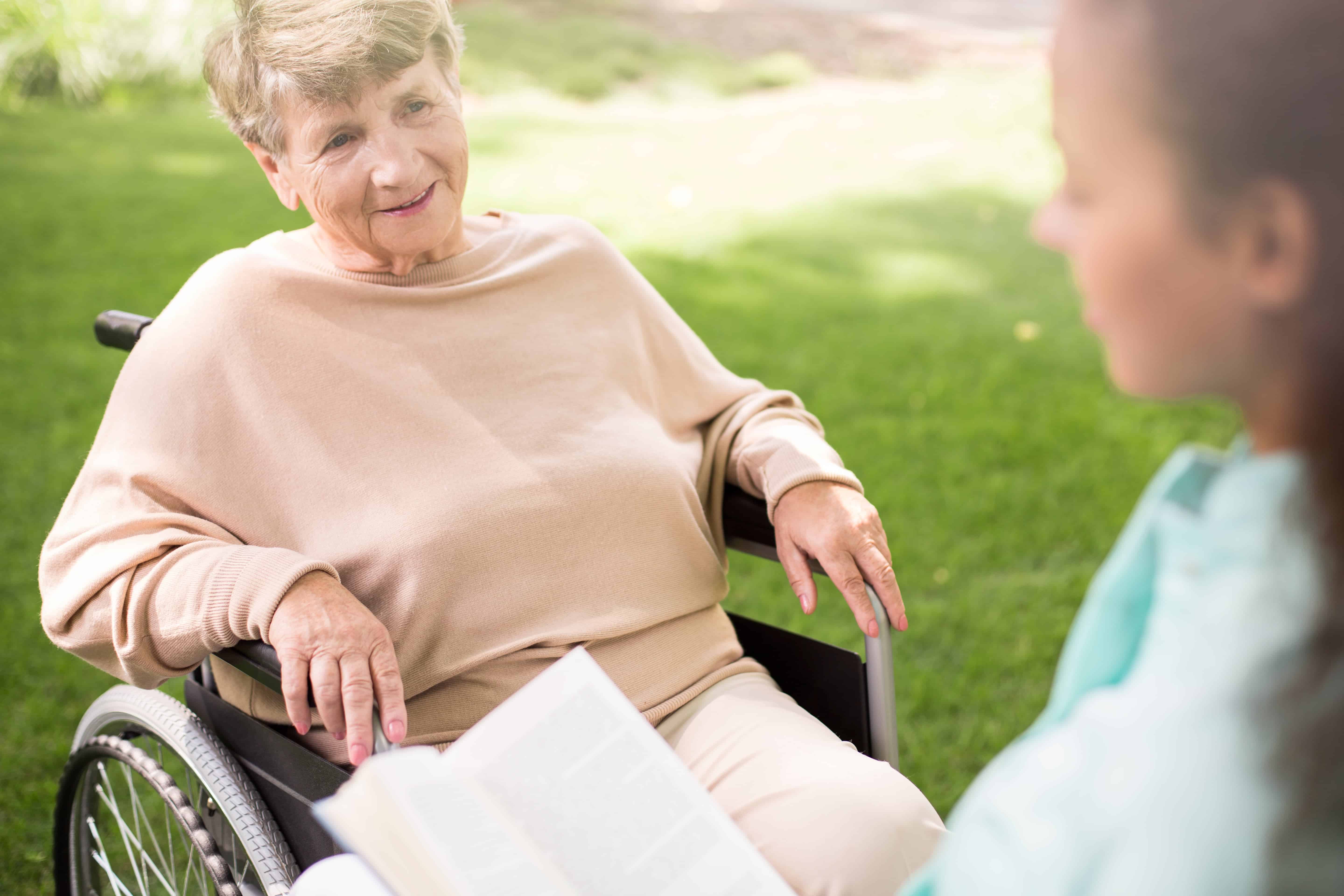 Smiling senior woman in wheelchair outside, facing younger woman