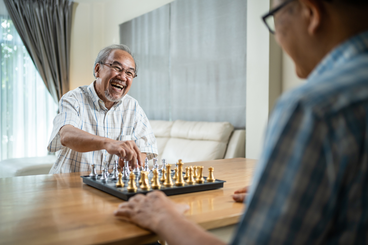 Asian Senior Elderly male spend leisure time, stay home after retirement. Happy smiling Old man enjoy activity in house playing chess game with friend together. Hospital Healthcare and medical concept