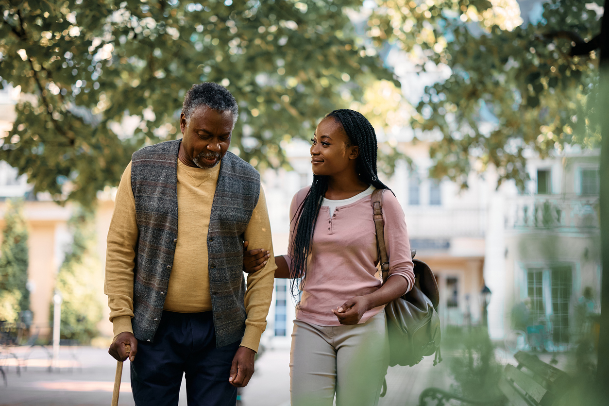 Happy African American woman walking with her senior father while visiting him at nursing home.