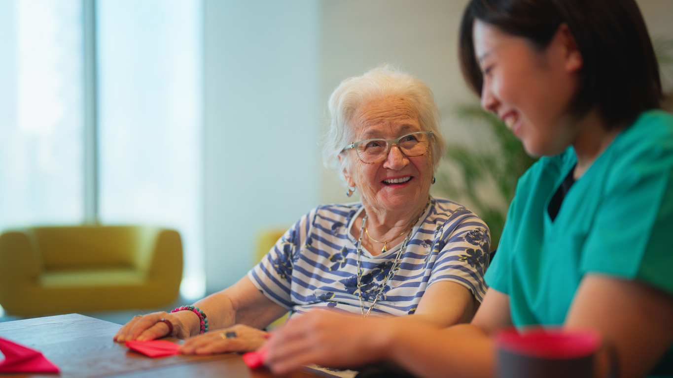 A senior woman is learning making origami as for physiotherapy activity.