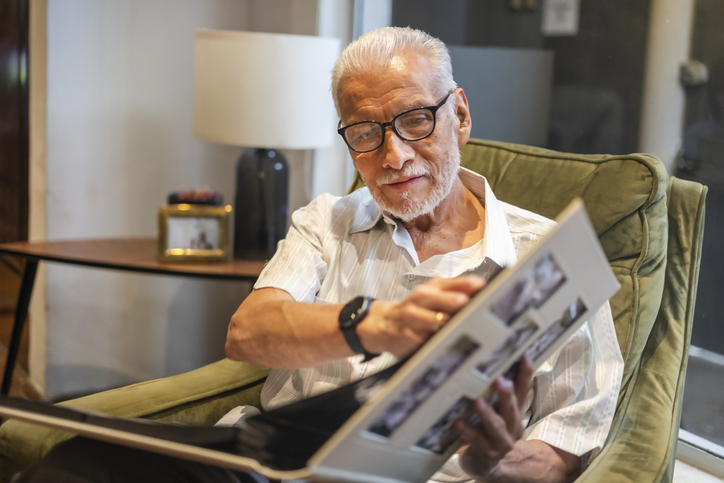 An elderly man looking at his photo album, reminiscing and reliving the good old days that are captured in photos throughout his life.